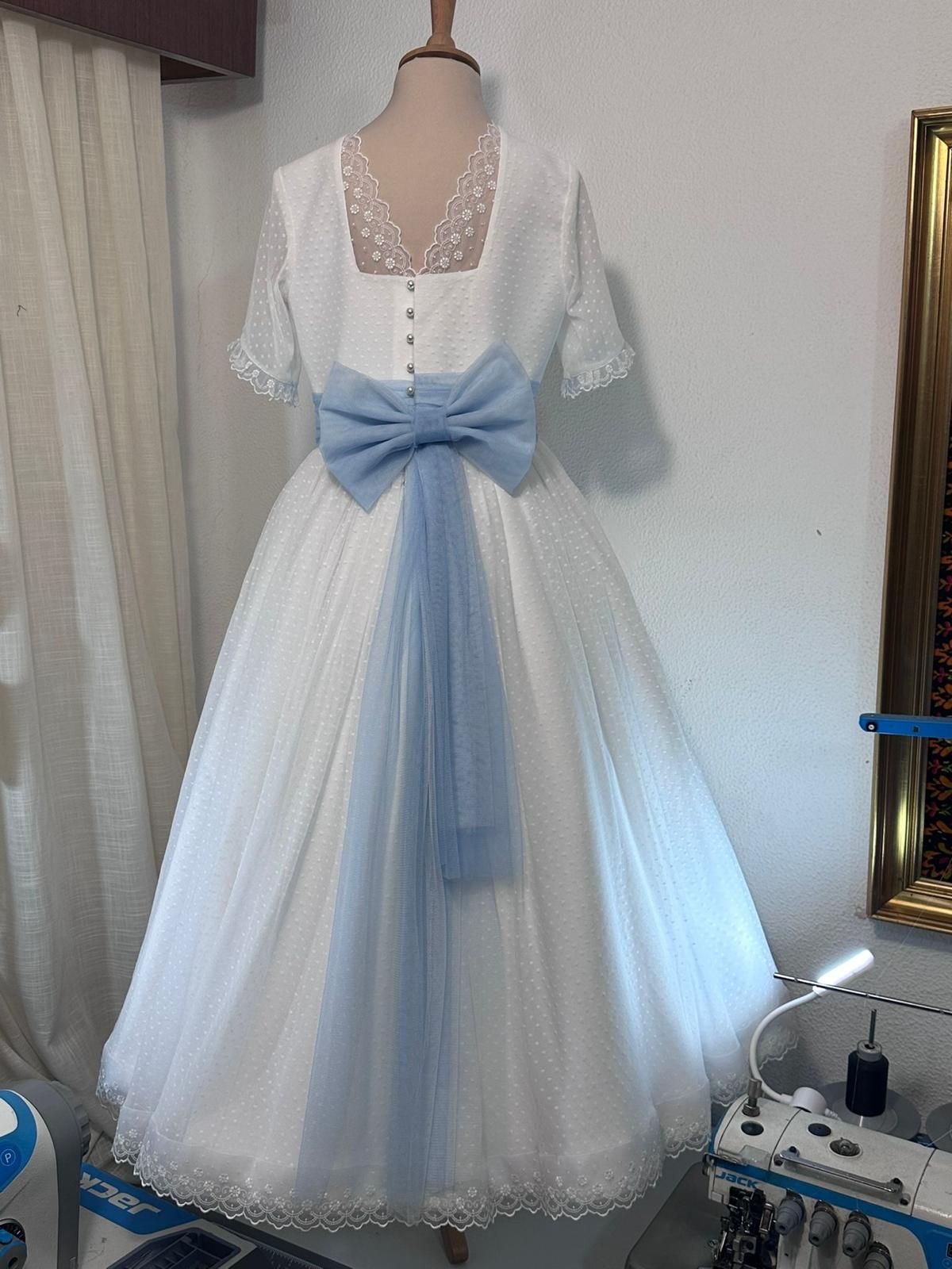 Un vestido blanco con un lazo azul en la espalda está sobre un maniquí.