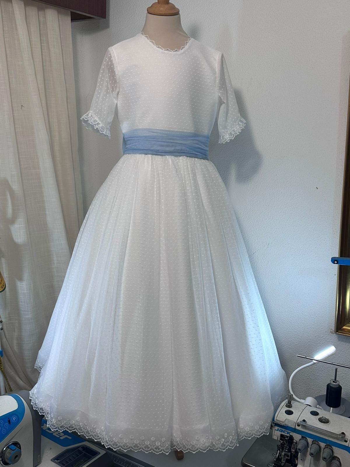 Un vestido blanco con una faja azul está sobre un maniquí.