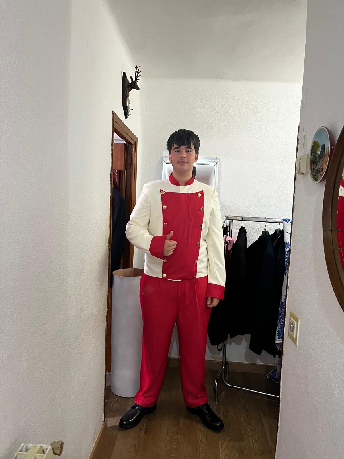 Un hombre con un traje rojo y blanco está parado en un pasillo haciendo un gesto de aprobación con el pulgar.