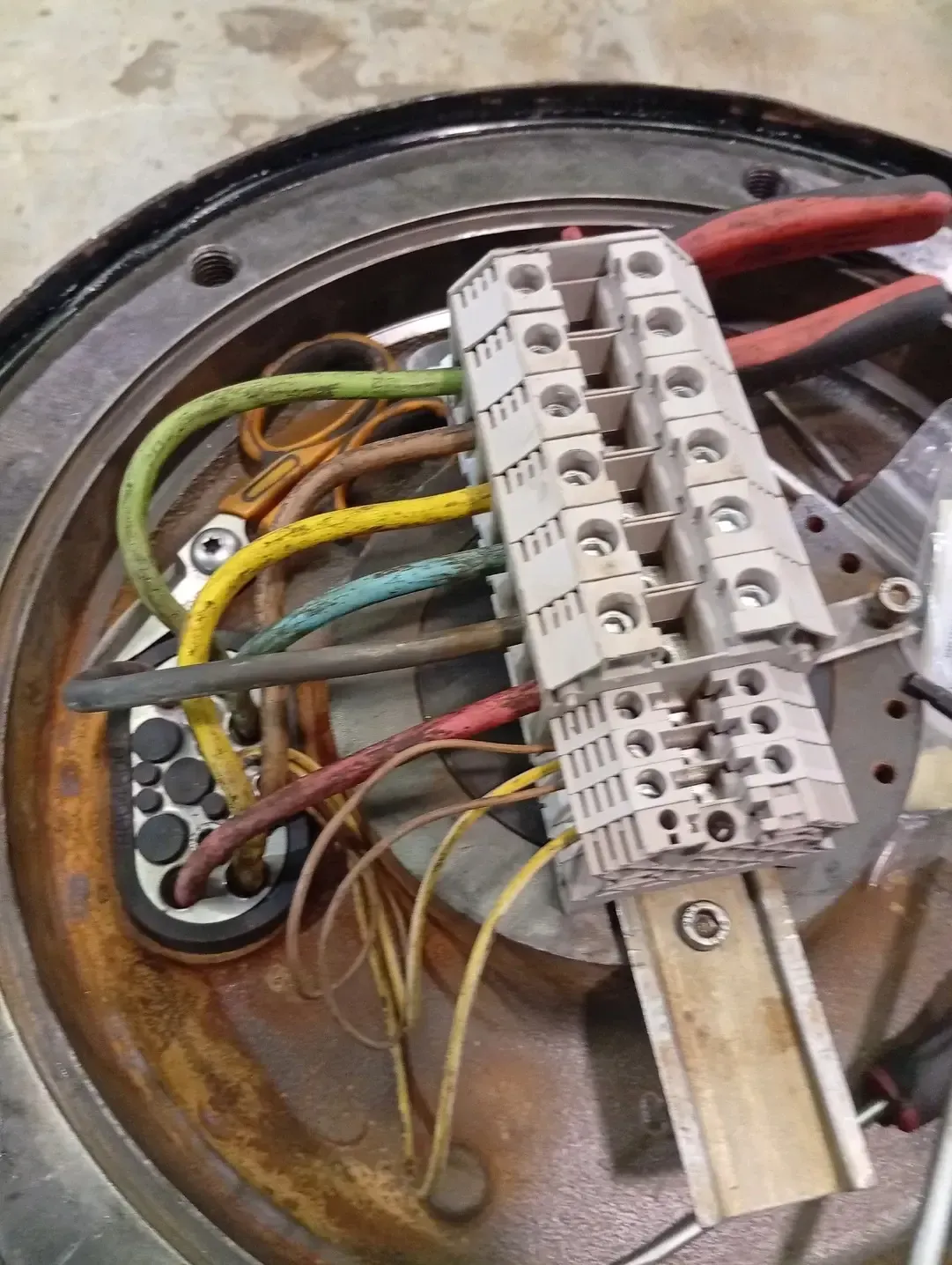 Cables eléctricos conectados a un bloque de terminales dentro de una carcasa de metal oxidado.