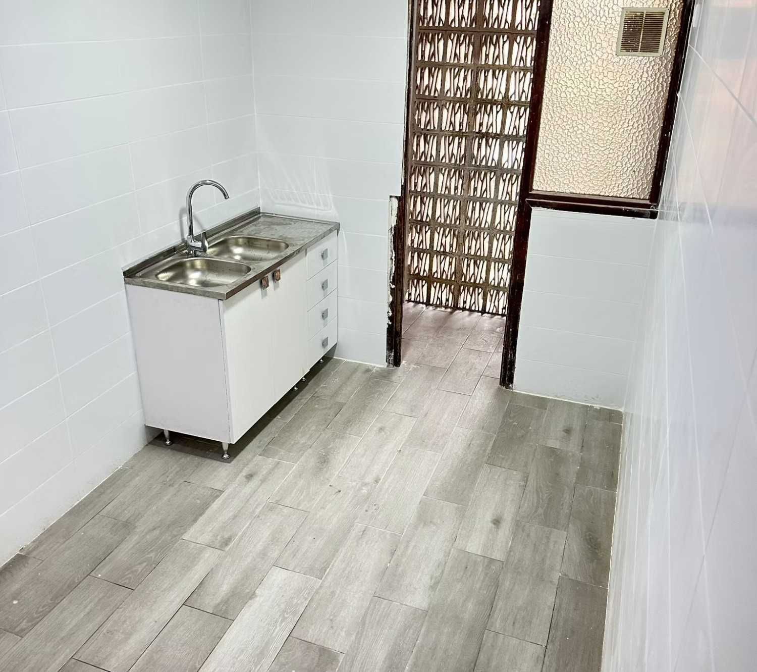 Cuarto de lavado blanco con mueble para lavabo, suelo de madera y puerta con panel decorativo.