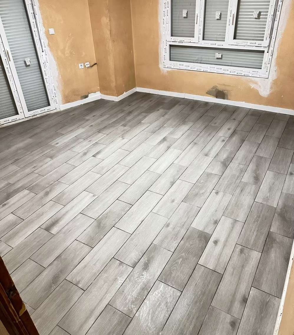 Habitación con suelo nuevo de imitación madera gris y paredes color canela sin terminar. Ventanas con molduras blancas.