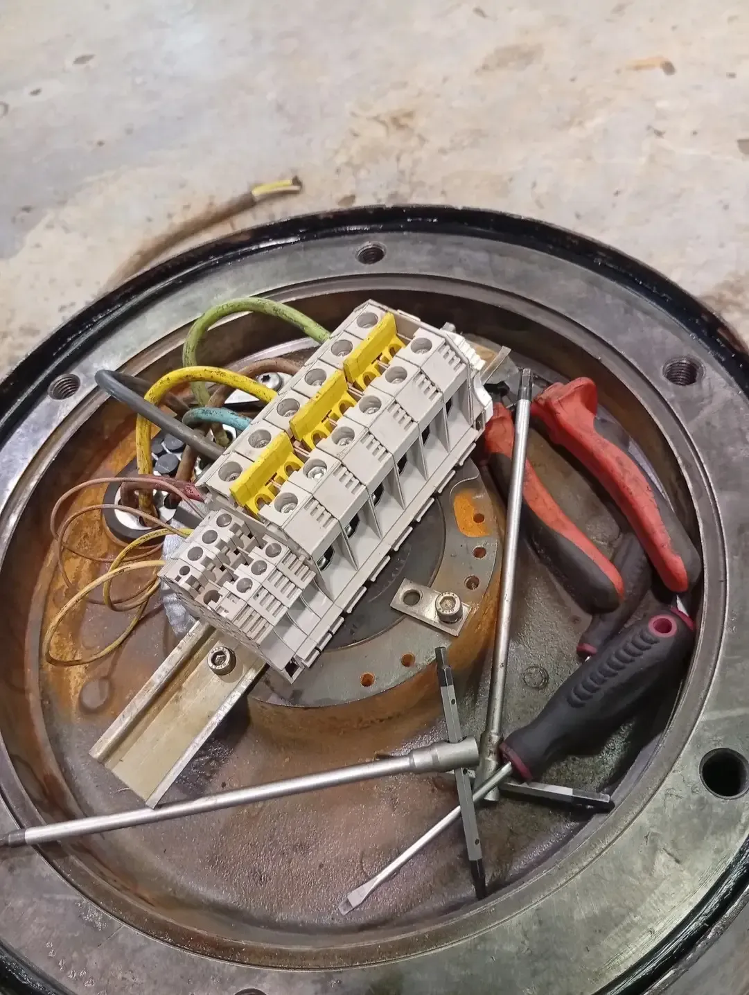 Caja de conexiones eléctricas abierta con cableado, bloques de terminales y herramientas.