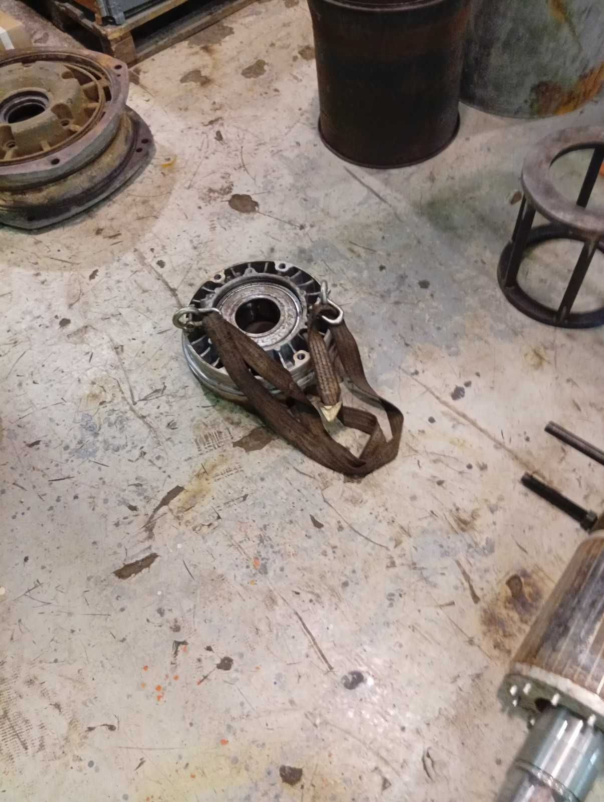 Un componente mecánico desmontado con correas sobre el suelo de hormigón de un taller. Otras piezas están dispersas.