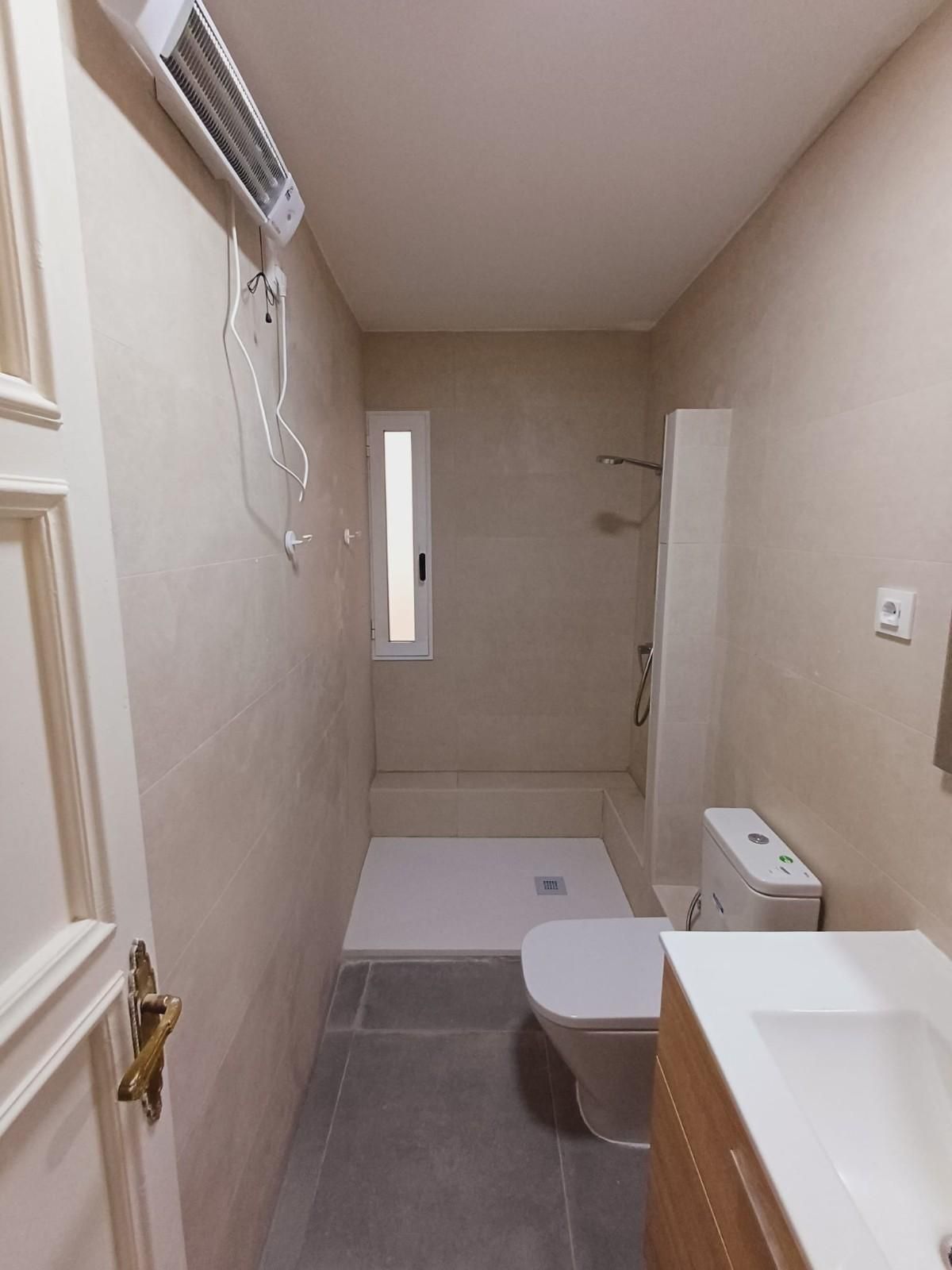 Baño pequeño y estrecho con inodoro, ducha, lavabo y calentador eléctrico.