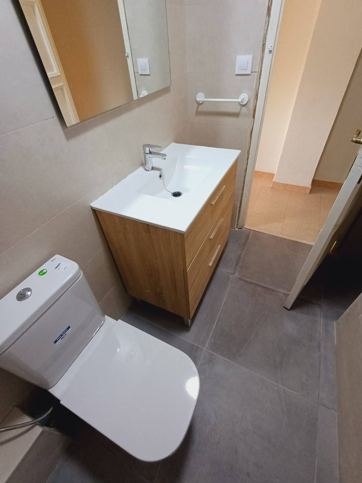 Baño con inodoro, lavabo y mueble. Suelo gris, paredes color canela y espejo.