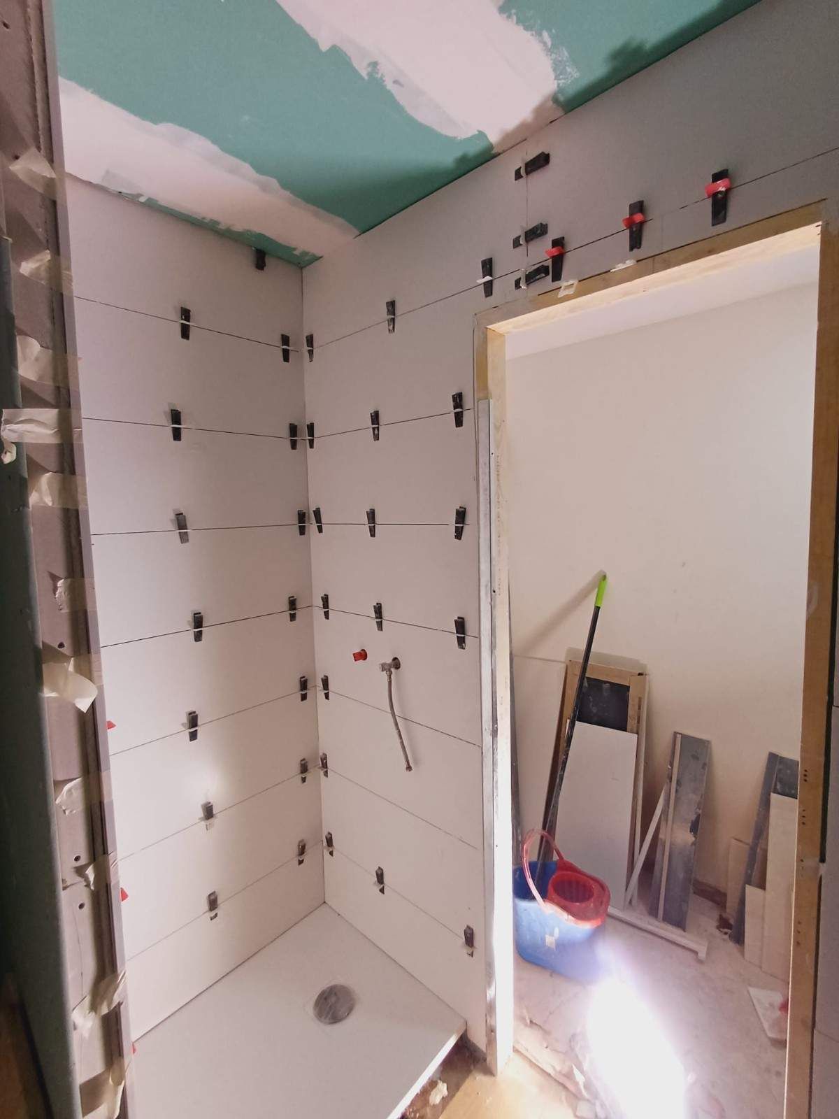 Baño en construcción, paredes revestidas con grapas niveladoras, puerta abierta, color blanco y verde.