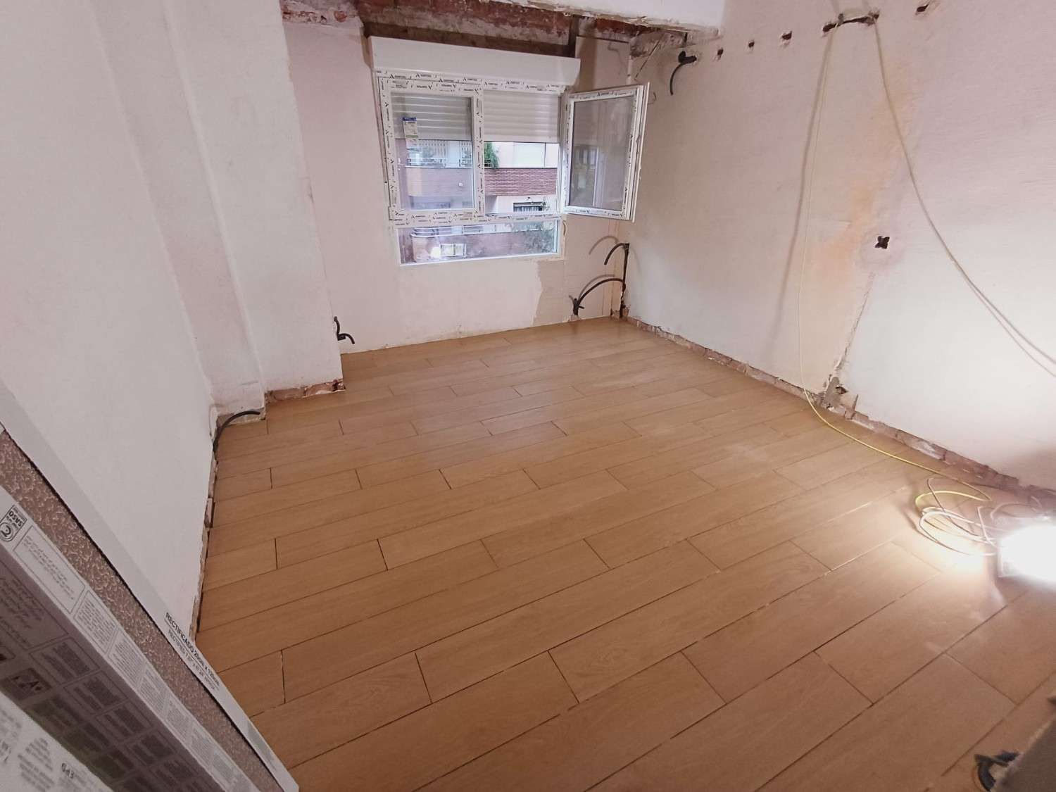 Habitación con piso nuevo imitación madera y paredes sin terminar; ventana visible.