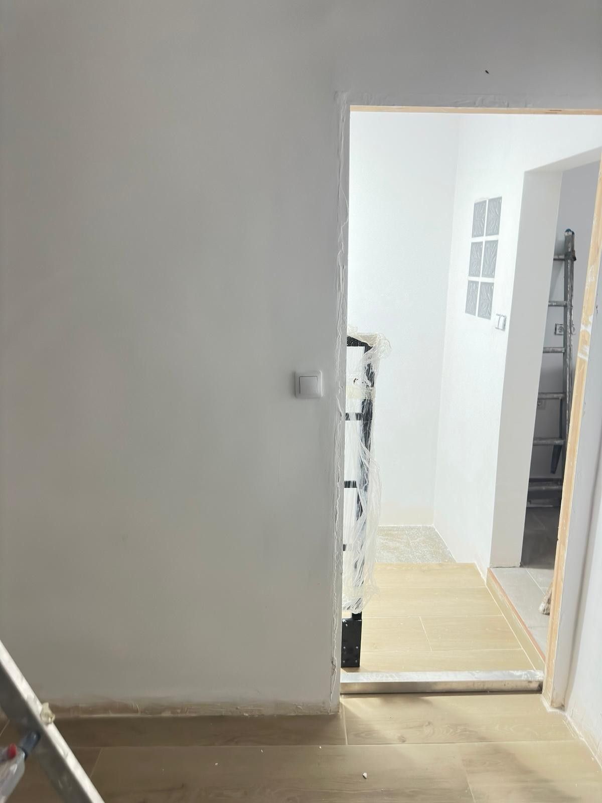 Puerta blanca que da a un pasillo con suelo de madera y escaleras. Hay un interruptor en la pared.