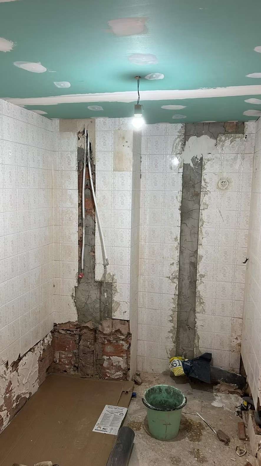 Baño en remodelación; tuberías y paredes expuestas, balde verde en el piso.