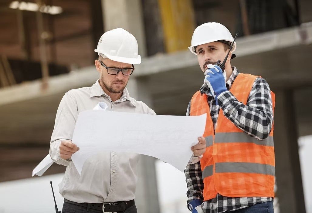 Dos obreros de la construcción revisando un plano que está en las manos de uno de ellos