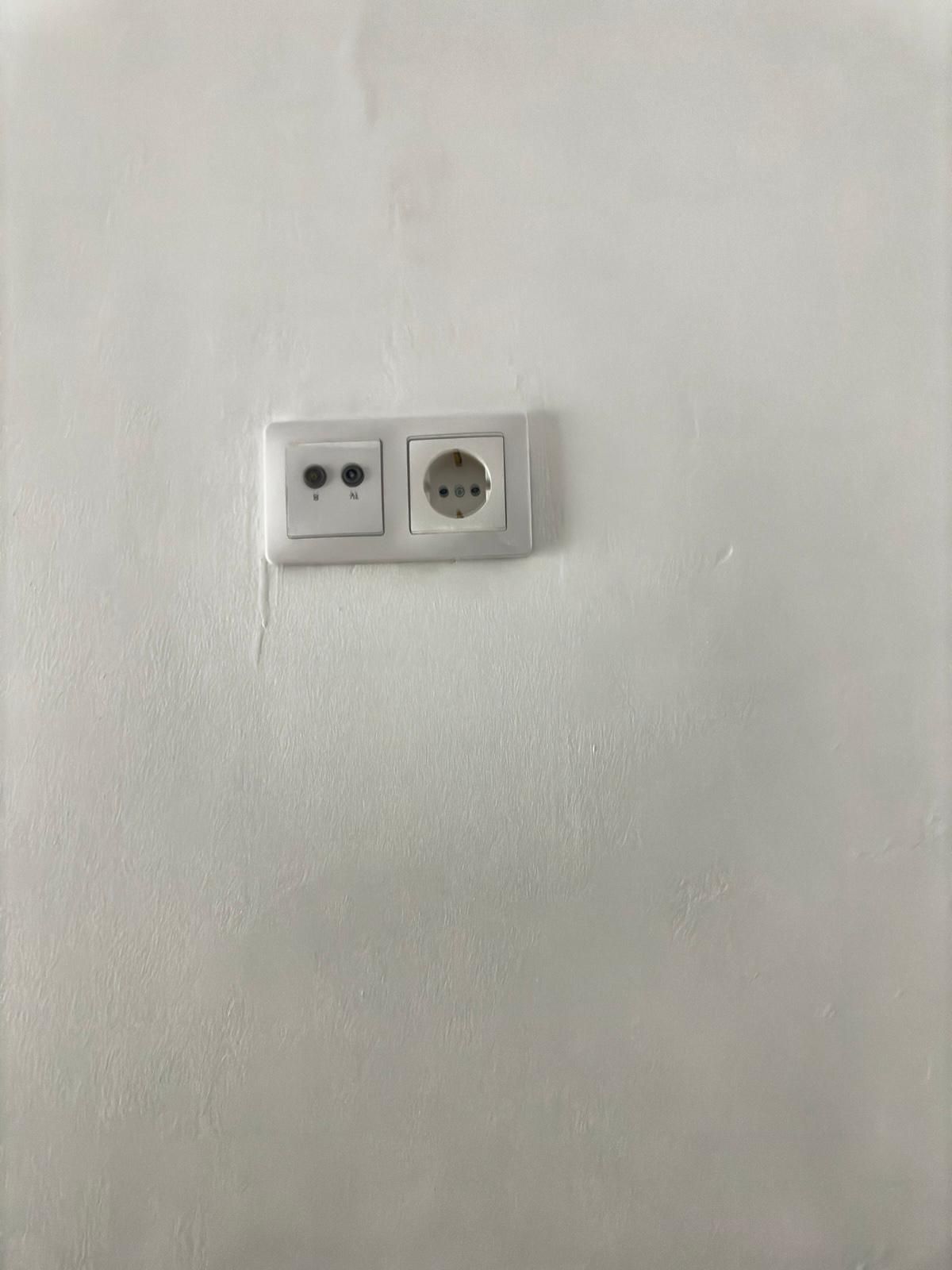 Pared blanca con dos tomas de corriente. Una es para un enchufe de dos clavijas y la otra, con toma de tierra.