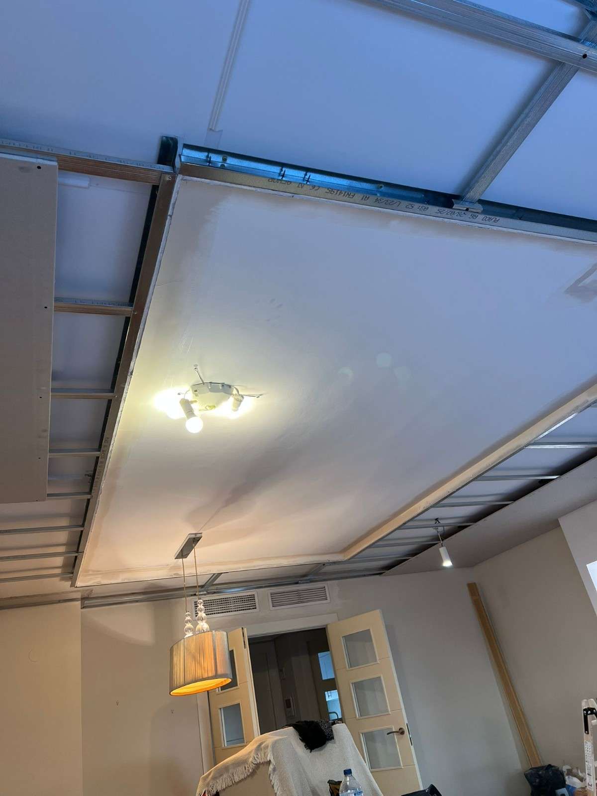 Techo con paneles de yeso parcialmente instalados, vigas de soporte de metal e iluminación empotrada.