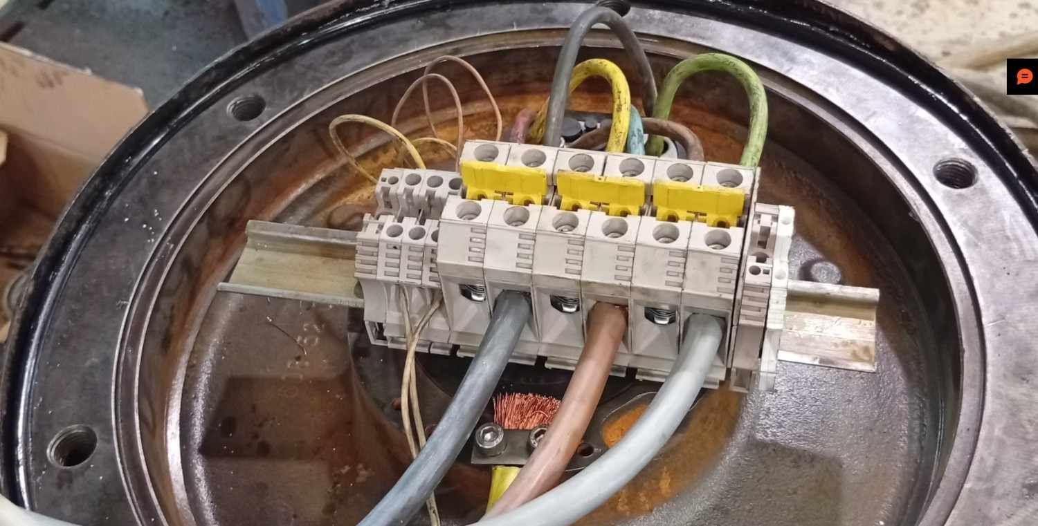 Bloque de terminales de cableado eléctrico con cables amarillos, verdes y grises dentro de una carcasa metálica.
