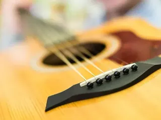 Primer plano del puente y las cuerdas de una guitarra acústica. Cuerpo de madera, puente negro, primer plano.