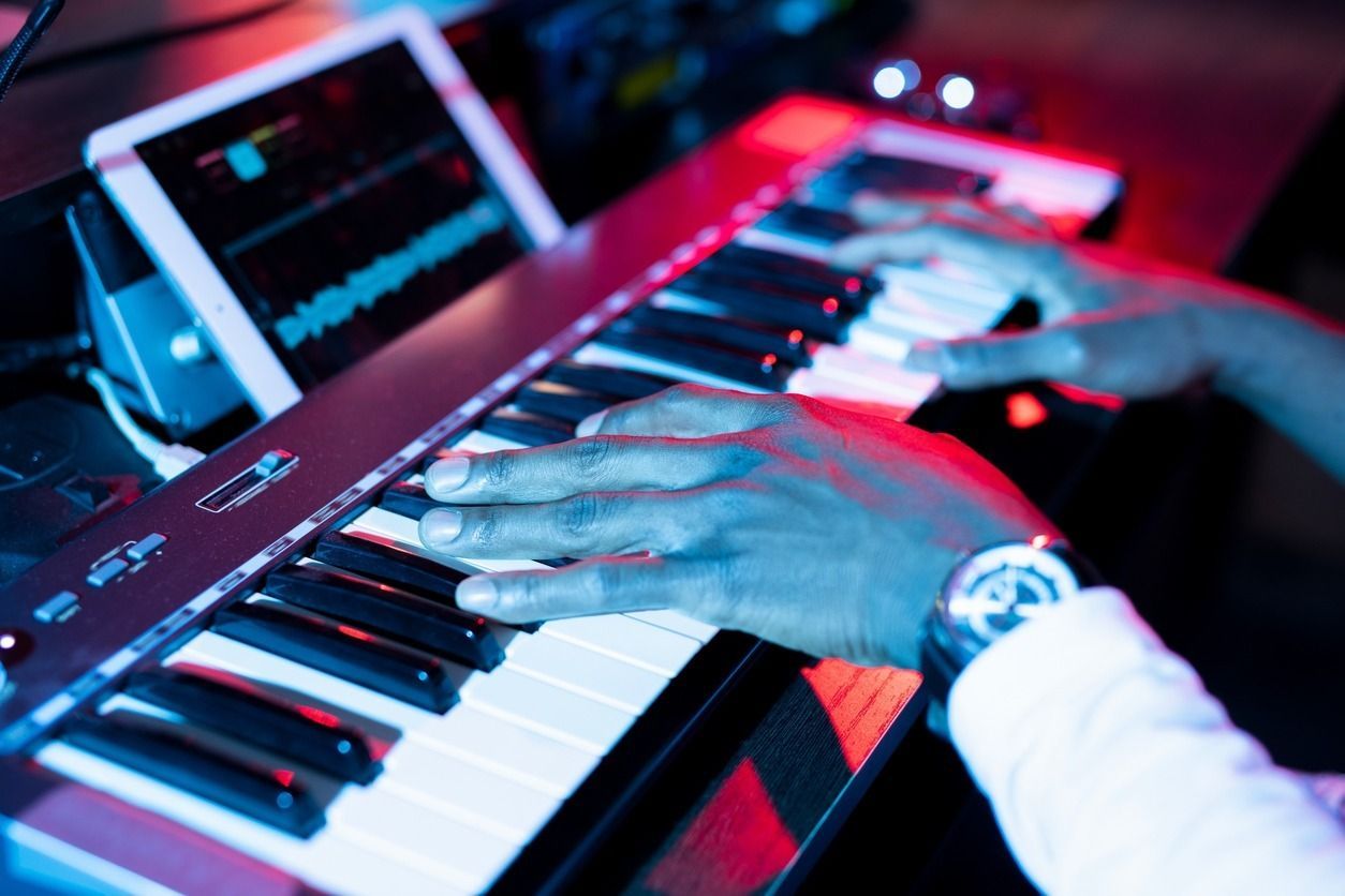 Persona tocando un teclado con las manos. Una tableta muestra formas de onda. Iluminación roja y azul.