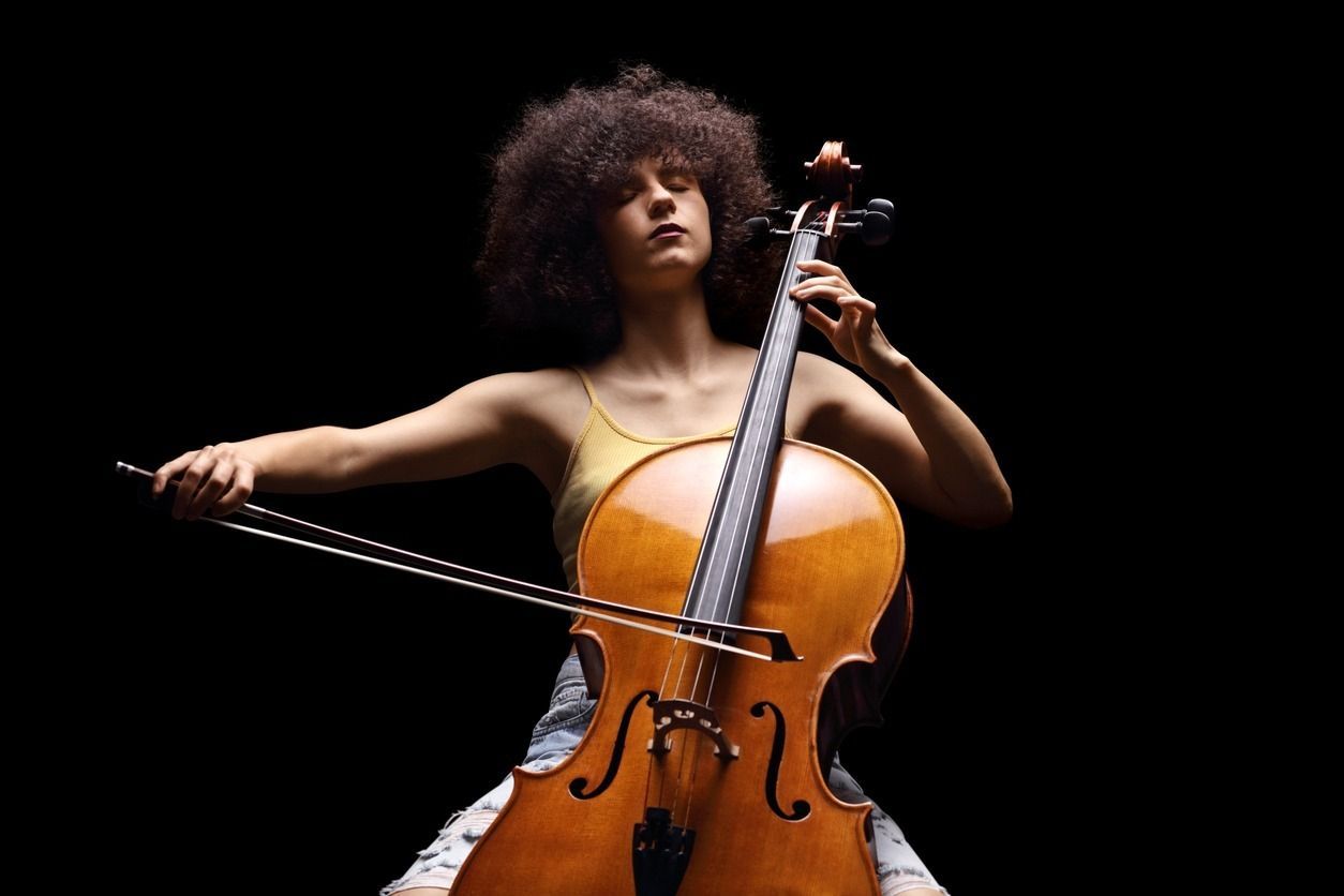 Mujer con cabello rizado tocando el violonchelo sobre un fondo negro.