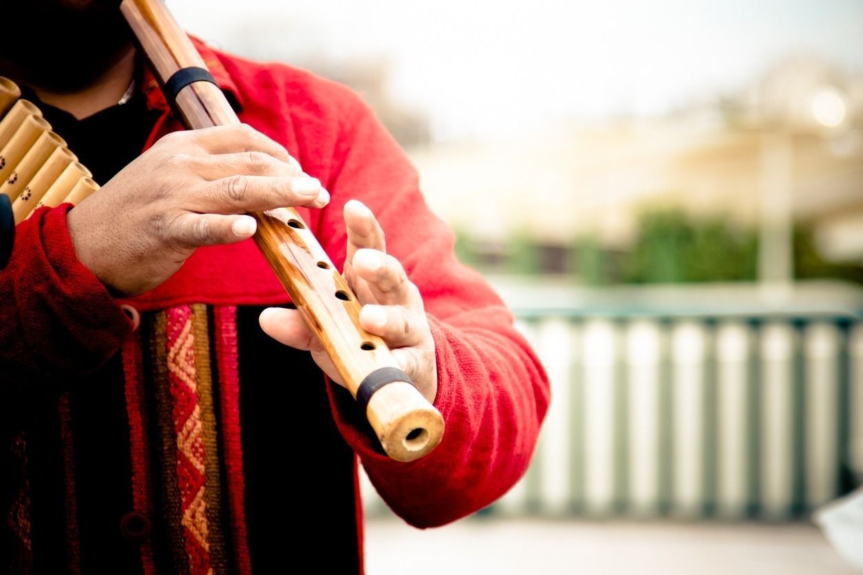 Persona tocando una flauta de madera, vestida con una camisa roja, al aire libre.