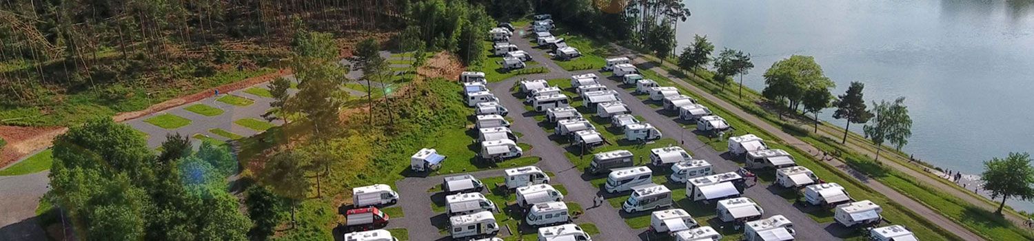 Eine Luftaufnahme einer Reihe von Wohnmobilen, die neben einem See geparkt sind.