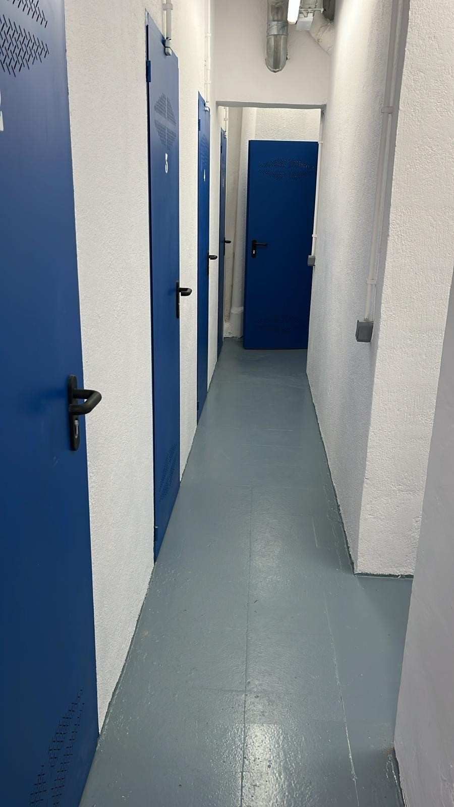 Pasillo estrecho con paredes azules y blancas, suelo gris y puertas azules a ambos lados.