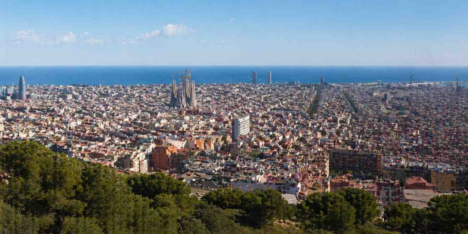 Paisaje urbano panorámico con edificios densos, un alto horizonte y el mar en el horizonte bajo un cielo azul.