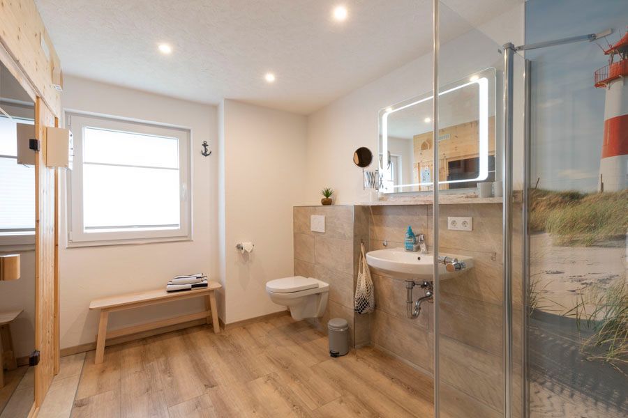 Ein Badezimmer mit Toilette, Waschbecken, Spiegel und ebenerdiger Dusche.