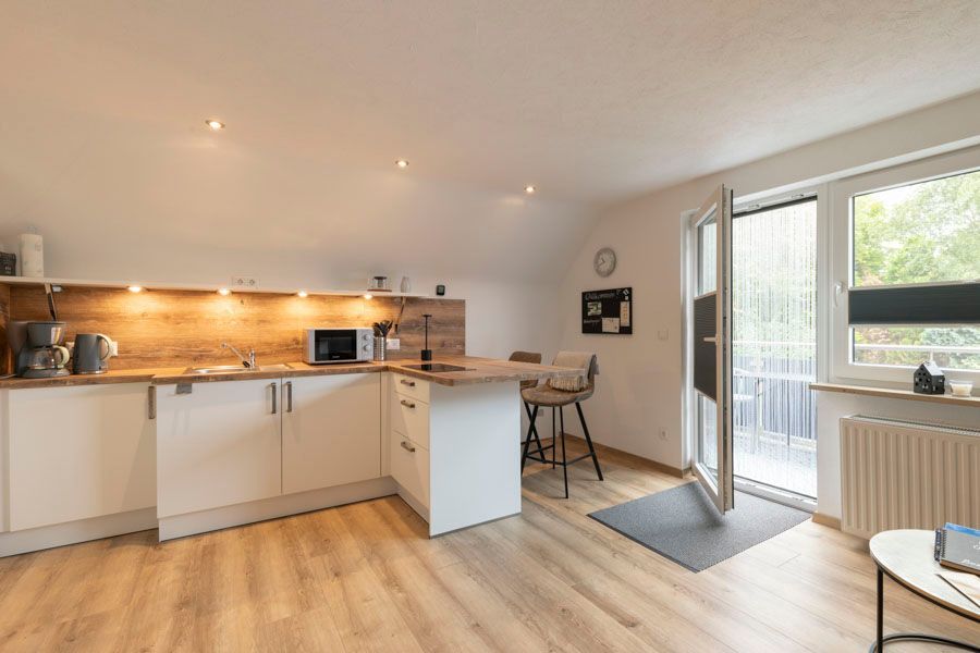 Eine Küche mit weißen Schränken und Holzböden in einem Wohnzimmer.