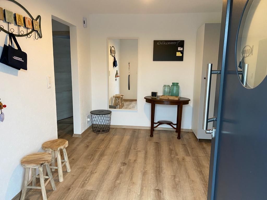 Ein Flur mit Holzboden, Hockern, einem Tisch und einem Spiegel.