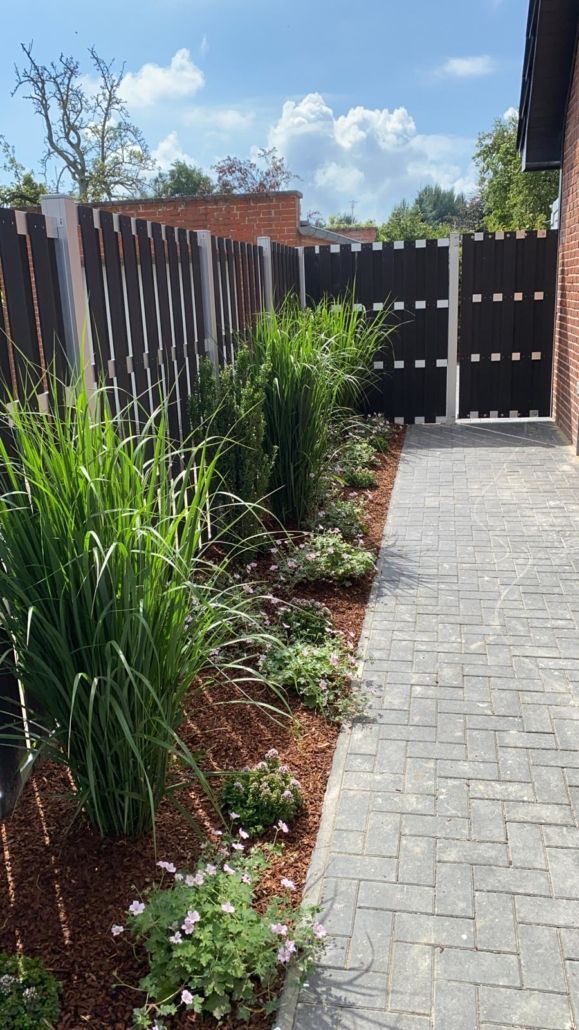 Ein Ziegelweg führt zu einem Haus mit Zaun und Pflanzen.