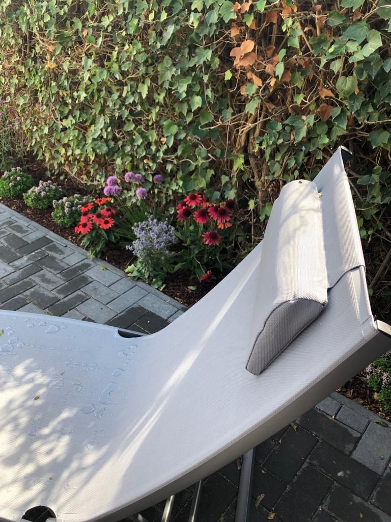 Ein weißer Stuhl steht vor einem Busch mit Blumen.