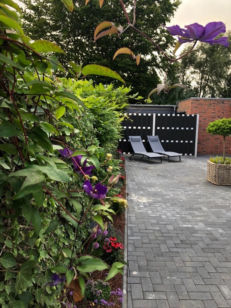 Ein Ziegelweg führt zu einer Terrasse mit Stühlen und Blumen.