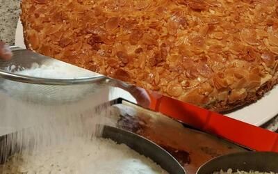 Eine Person siebt Zucker in eine Pfanne neben einem Kuchen.