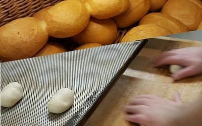 Eine Person rollt Teig auf einem Tablett neben einem Korb mit Brötchen aus.