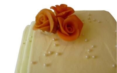 Eine weiße Torte mit orangen Rosen und Perlen obenauf