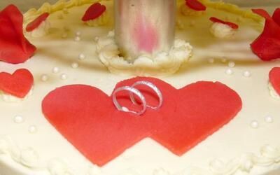 Eine Hochzeitstorte mit zwei roten Herzen und zwei Eheringen obendrauf.