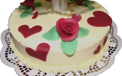 Ein weißer Kuchen mit roten Herzen und einer Rose obendrauf.