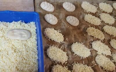 Ein blaues Tablett mit geriebenem Käse neben einem Bündel Brot auf einem Tisch.