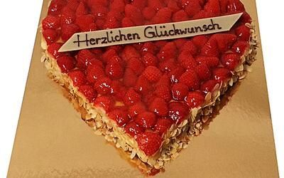 Ein herzförmiger Kuchen mit Himbeeren und einem Schild mit der Aufschrift „Herzlichen Glückwunsch“