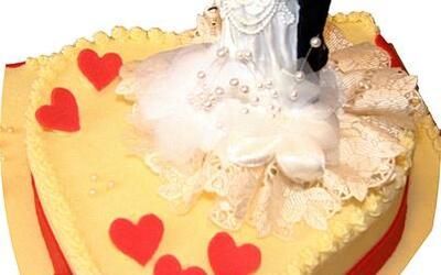 Eine herzförmige Hochzeitstorte mit einer Braut- und Bräutigamfigur oben drauf.