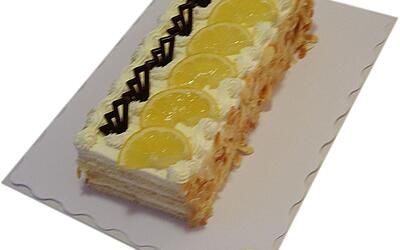 Ein langer Kuchen mit Zitronenscheiben und Schlagsahne auf einem weißen Teller.
