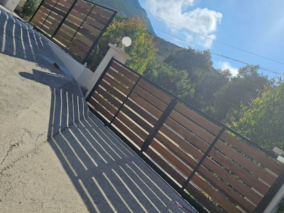 Portail en bois et métal noir sur une allée en béton avec toile de fond de montagne.