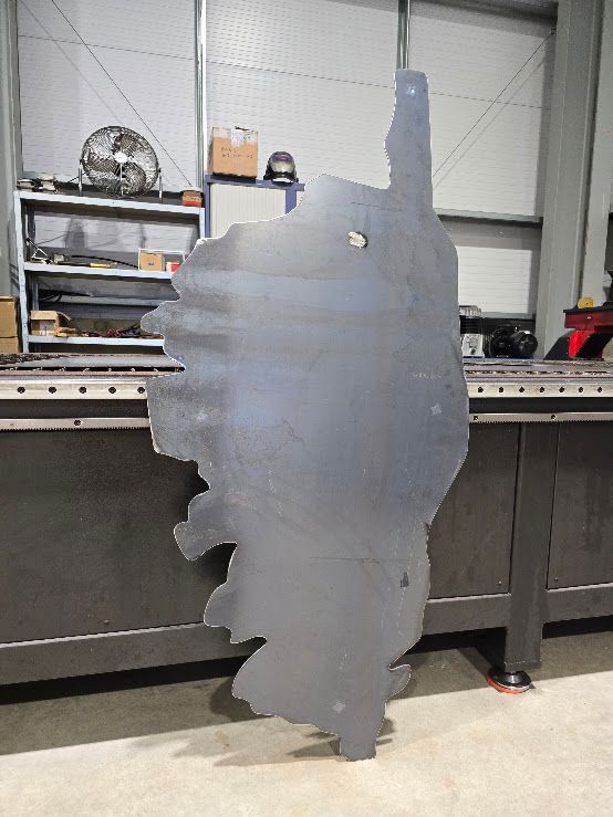 Découpe métallique de l'île de Corse, debout dans un atelier avec des équipements industriels en arrière-plan.