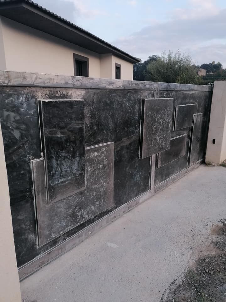 Portail en métal sombre avec des motifs géométriques abstraits devant une maison de couleur claire.