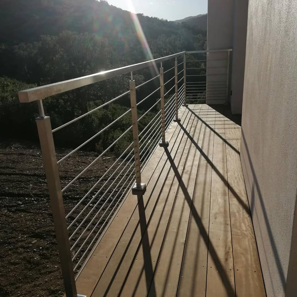 Garde-corps en acier inoxydable sur une terrasse en bois, projetant de longues ombres avec un arrière-plan de montagne.