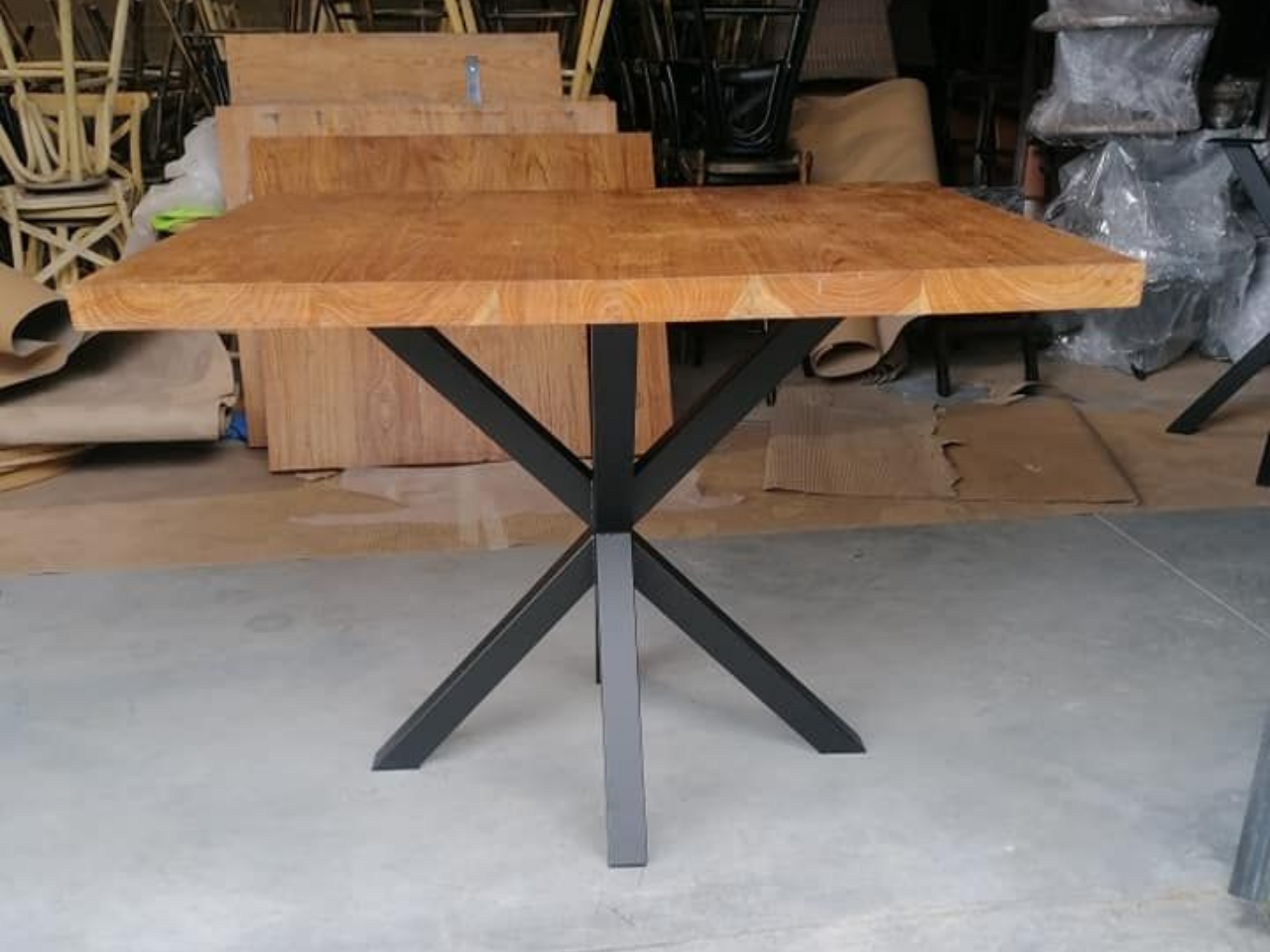 Table carrée en bois avec un piètement en métal noir en forme de X.