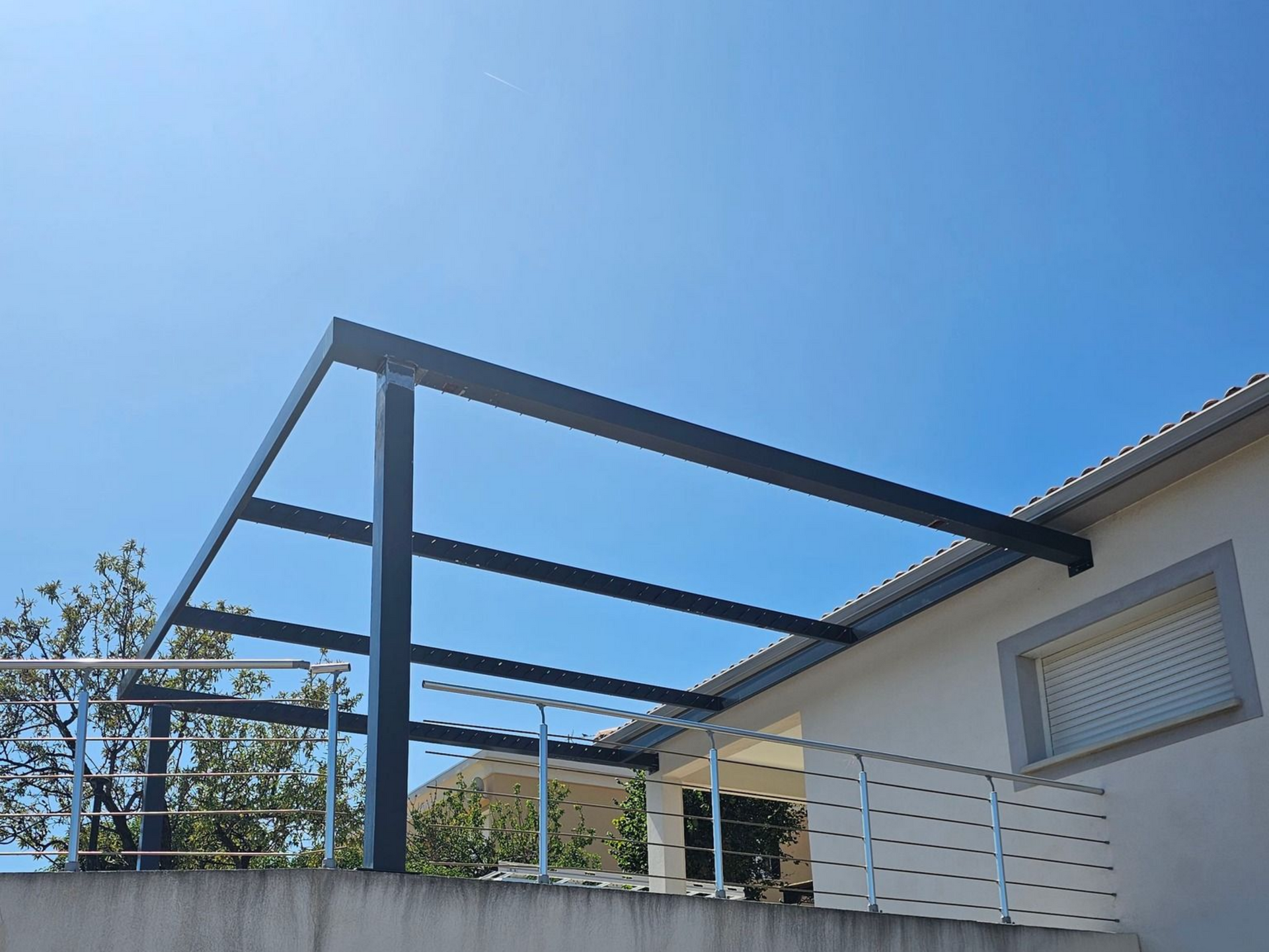 Structure de pergola noire sur un balcon contre un ciel bleu vif.