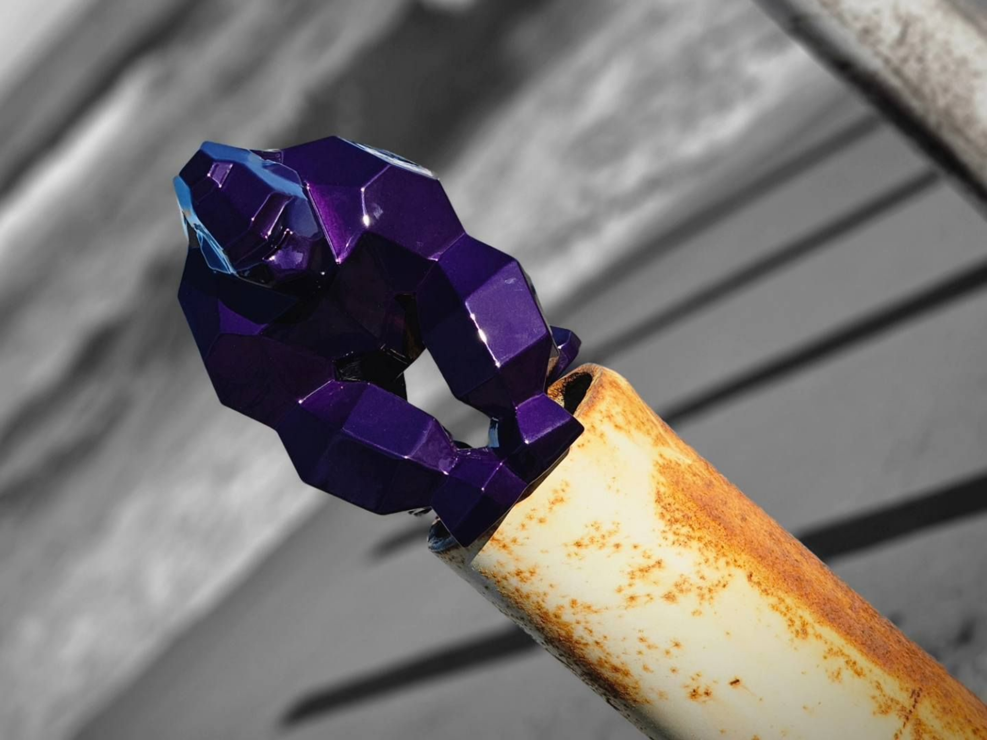 Gorille violet à facettes sur un tuyau en métal rouillé sur un fond noir et blanc.