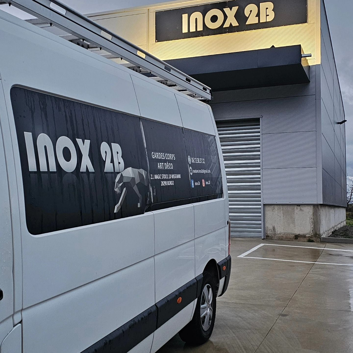 Camionnette blanche avec logo INOX 2B garée devant un bâtiment portant le même logo.