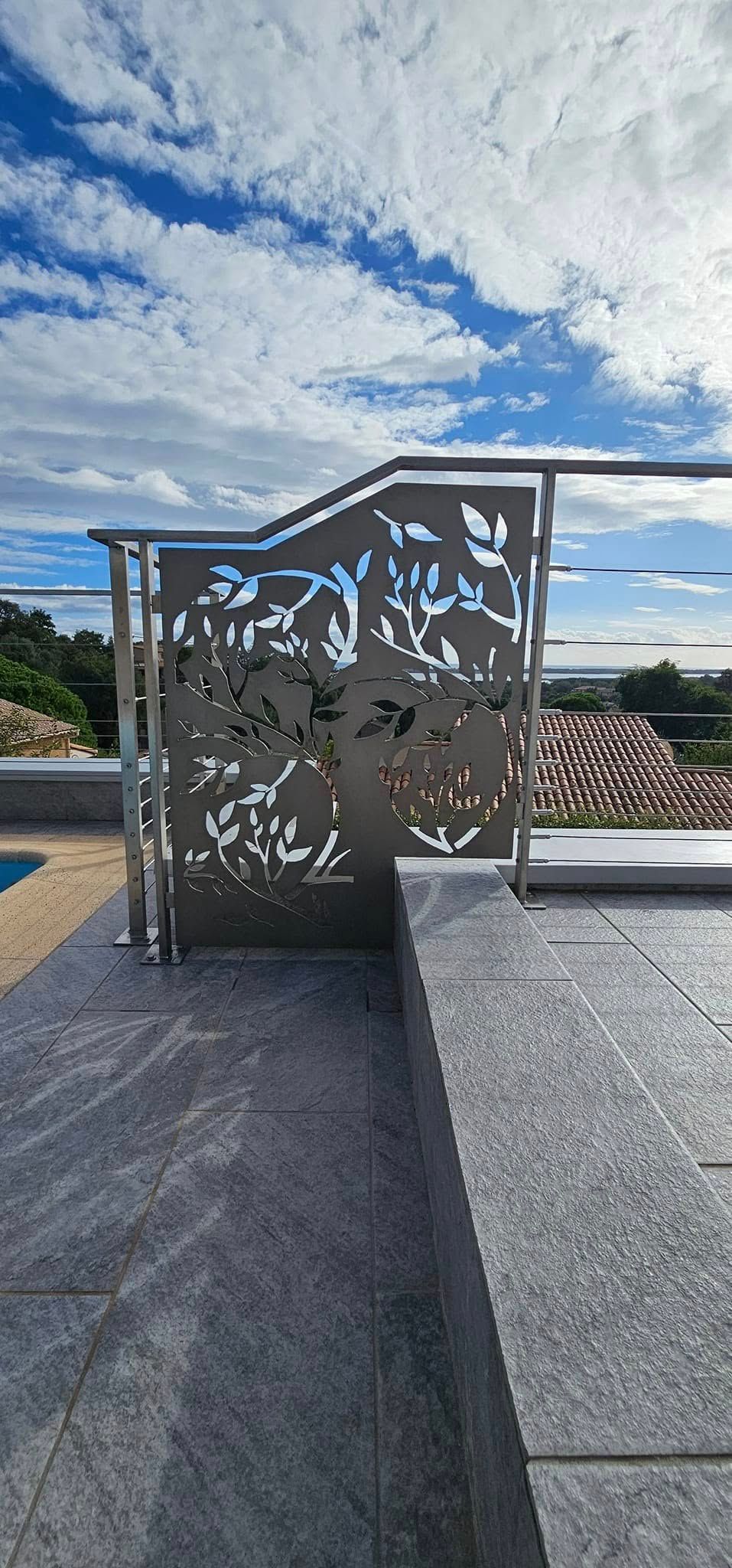 Clôture décorative en métal avec découpes de feuilles, décor de toit, contre un ciel bleu.