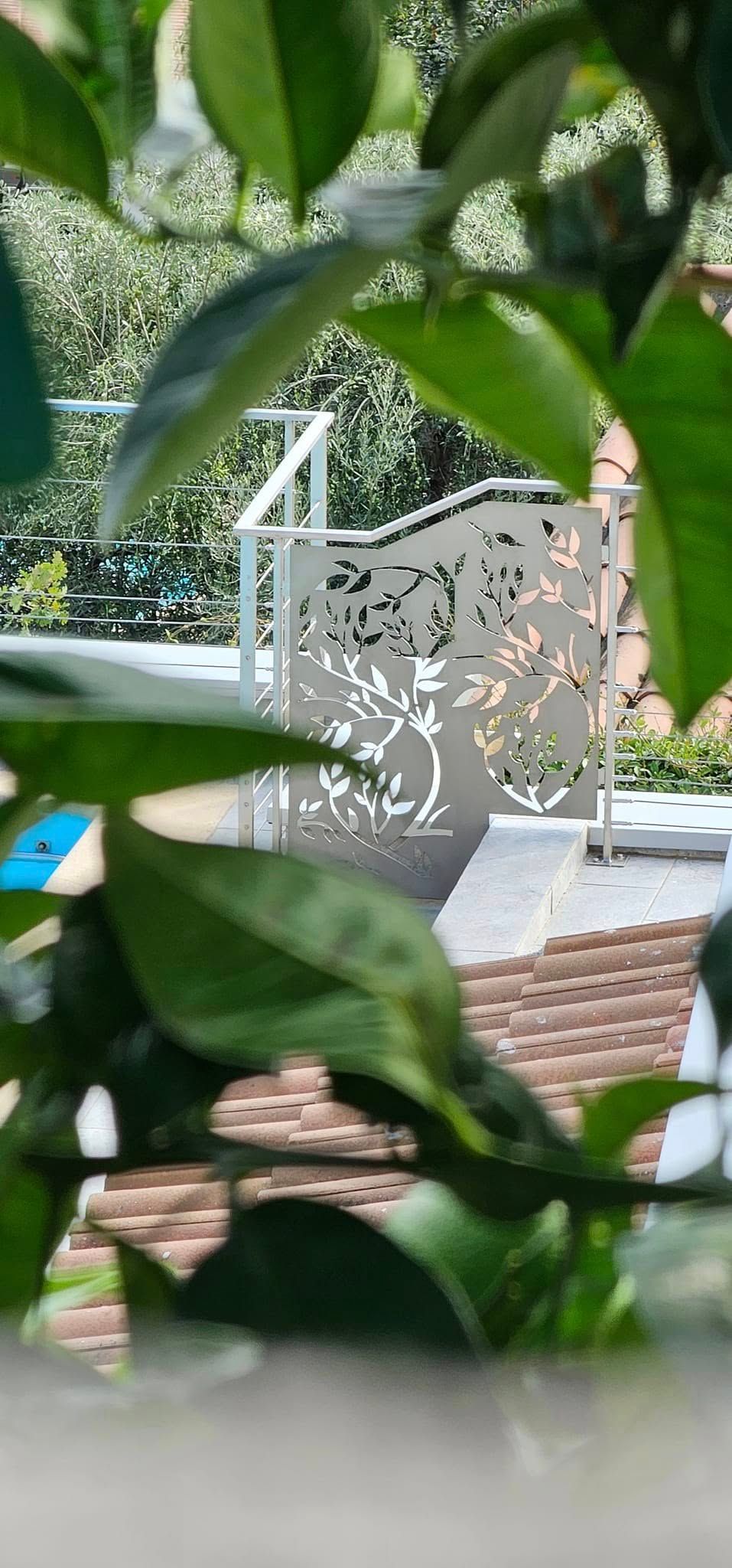 Clôture blanche avec des découpes d'arbres, vues à travers des feuilles vertes ; cadre extérieur ensoleillé.